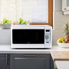 a white microwave oven sitting on top of a counter next to a bowl of fruit