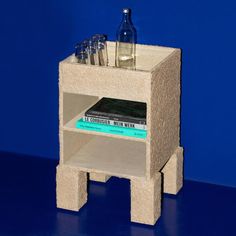 a book shelf made out of concrete with books and bottles on top in front of a blue wall