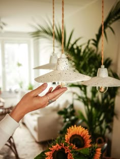 a person is holding two lamps in their hand and some flowers are on the table