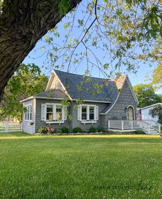 a gray house sitting on top of a lush green field next to a large tree