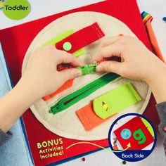 a child's hands holding scissors on top of a book with other toys in the background