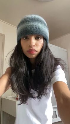 a woman with long hair wearing a knitted hat and looking at the camera while standing in front of a microwave