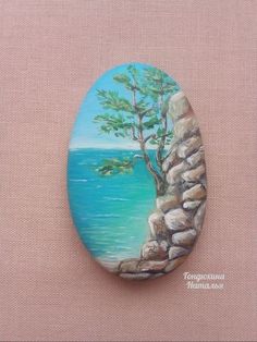 a painted rock with a tree on the rocks by the ocean is shown in this image