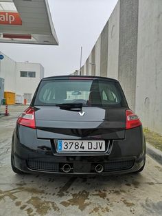 the back end of a black car parked in front of a gas station with no one around