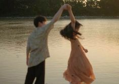 a man and woman are dancing in the water at sunset or sunrise, with trees in the background