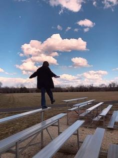 a person jumping in the air over several picnic tables on a field with blue skies and white clouds