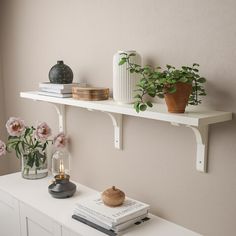 two white shelves with books and vases on them, one shelf is holding flowers