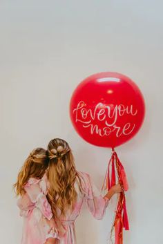 two girls are holding a red balloon with the words love you more written on it