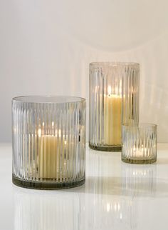 two clear glass candles sitting next to each other on a white counter top with reflections