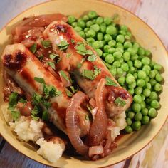 a yellow plate topped with meat and vegetables next to green peas on top of a wooden table