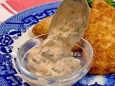 a blue and white plate topped with fried chicken covered in gravy next to a dipping sauce