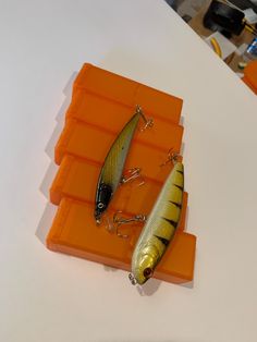 two fishing lures sitting on top of orange trays