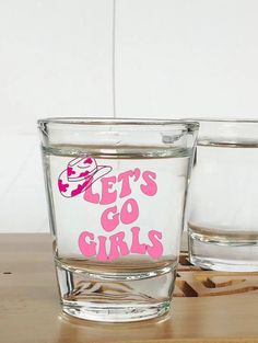 two glasses with pink lettering on them sitting on top of a wooden table next to each other