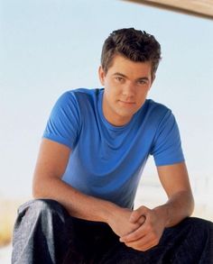 a young man sitting on the ground wearing a blue shirt