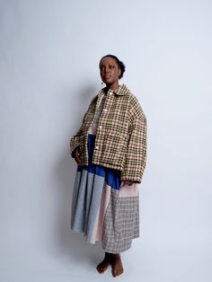 a woman standing in front of a white wall wearing a plaid jacket and pleated skirt