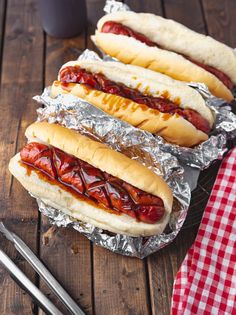 two hot dogs with ketchup and mustard sitting on tin foil next to a drink