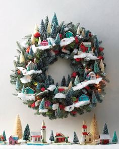 a christmas wreath is hanging on the wall next to small trees and snow covered houses