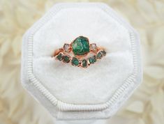 an emerald and diamond ring sitting on top of a white velvet covered cushioned box