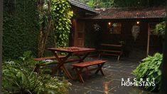 a wooden table and bench in front of a house with plants on the outside wall