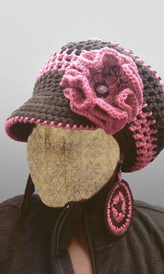 a woman wearing a crocheted hat with pink flowers on the brim and earring