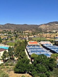 an aerial view of a tennis court surrounded by trees and mountains in the distance,