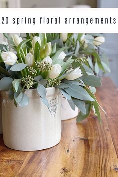 two white vases filled with flowers sitting on top of a wooden table next to each other