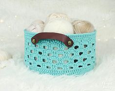 a blue crocheted basket with balls of yarn in it on a white furnishing