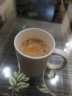 a white cup filled with liquid on top of a glass table next to a wall