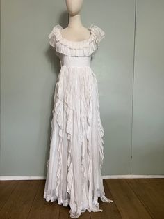 "Absolutely gorgeous white long 70s cotton dress. Has a scooped neckline with a double tiered frill that can be worn off the shoulders, a waist seam that measures 30\" and a long floaty skirt with vertical tiers along the length of the skirt. Fastens not he side with buttons. Fully lined in white cotton and has well constructed bodice for better fit and comfort. Would make a fabulous wedding dress! Size UK 8/10" White Tiered Ruffle Maxi Dress, White Maxi Dress With Ruffled Skirt, White Tiered Maxi Dress With Ruffles, White Tiered Dress With Ruffles, White Ruffled Tiered Dress For Garden Party, White Tiered Ruffle Dress For Garden Party, White Tiered Ruffle Dress, White Tiered Ruffle Dress For Wedding, White Tiered Skirt Maxi Dress With Ruffles