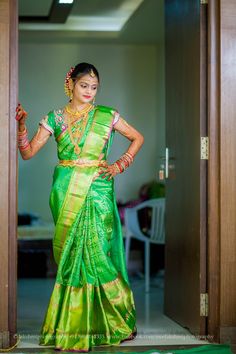 a woman in a green and gold sari is posing for the camera with her hands on her hips