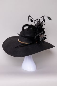 The Pure Elegance Derby Hat embodies timeless sophistication with its sleek design and luxurious materials. Adorned with subtle embellishments of feathers, flowers, and a beautiful gold chain, it adds a touch of glamour to any outfit. Versatile and refined, this hat is perfect for derby events, weddings, or garden parties, making a memorable statement with its understated charm and impeccable style. NO RETURNS/EXCHANGES due to the nature of the product (special occasions and headwear). Not all s Elegant Black Fascinator For Evening, Elegant Feathered Fascinator For Party, Elegant Feather Fascinator For Party, Elegant Party Fascinator With Feather Trim, Black Feathered Evening Hat, Luxury High Crown Hat For Formal Occasions, Evening Fascinator With Feather Trim, Elegant Evening Fascinator With Feather Trim, Elegant Black Party Hat