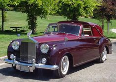 an old fashioned car parked in a parking lot next to a park with benches and trees