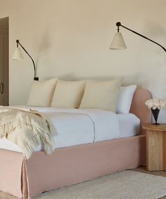 a bed with white sheets and pillows in a bedroom next to a lamp on the wall