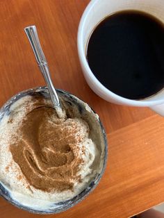 two cups of coffee sit next to each other on a wooden table with spoons