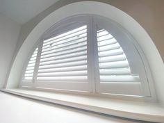 an arched window with white shutters in the corner