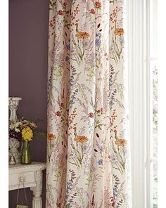 the curtains in this room are made with floral print and have purple walls, along with a white table