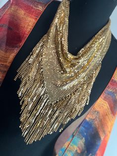 ### Gold Metal Mesh 1970s Style Bandana Necklace Scarf - Disco-Inspired Body Jewelry Embrace the glamour and sparkle of the 1970s with our Gold Metal Mesh Bandana Necklace Scarf. This dazzling piece combines the bold style of a bandana with the elegance of body jewelry, creating a statement accessory perfect for any disco-inspired look. ### Features: - **Design Triangular cowl design reminiscent of 1970s disco fashion, crafted to drape elegantly around the neck and shoulders. - **Materials Shimmering gold metal mesh that catches the light beautifully, adding a touch of vintage glamour. - **Versatile Wear Can be worn as a necklace, scarf, or body jewelry, making it a versatile addition to your accessory collection. - **Comfort Lightweight and flexible mesh material ensures a comfortable fit Vintage Party Choker With Adjustable Chain, Glamorous Festival Jewelry With Chain Detail, Costume Jewelry Chain Necklaces For Festivals, Vintage Jewelry With Adjustable Chain For Party, Vintage Party Jewelry With Adjustable Chain, Vintage Choker Chain Necklace For Party, Bohemian Party Jewelry With Chain Detail, Glamorous Metal Jewelry For Festival, Bohemian Party Jewelry With Chain