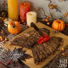 a cutting board topped with meat next to candles and pumpkins