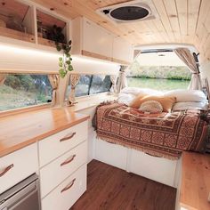 the interior of a camper with wood flooring and white furniture, including a bed