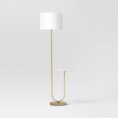 a lamp with a white shade on it and a gold stand in front of the light