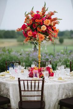 the table is set with white linens and colorful flowers in vases on it