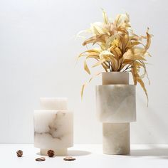 two marble vases with flowers in them on a white table next to each other