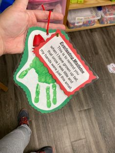 a person holding up a handprinted christmas ornament that reads, there is something green and red