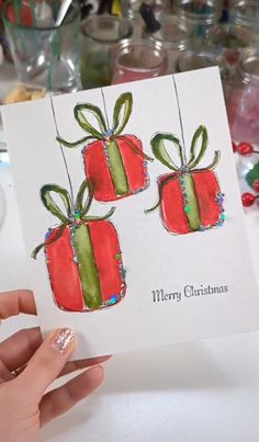 a hand holding up a card with two wrapped presents on it and the words merry christmas