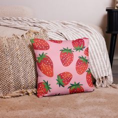 a pink pillow with strawberries on it next to a white and black striped blanket