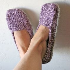 a person's feet with crocheted slippers on, against a white wall