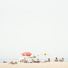 several people sitting on the beach under umbrellas