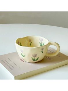 a white bowl with flowers painted on it sitting on top of a book next to a cup