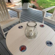 a white table sitting on top of a wooden deck next to two chairs and a potted plant