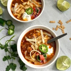 two bowls of chili soup with tortilla strips and limes on the side